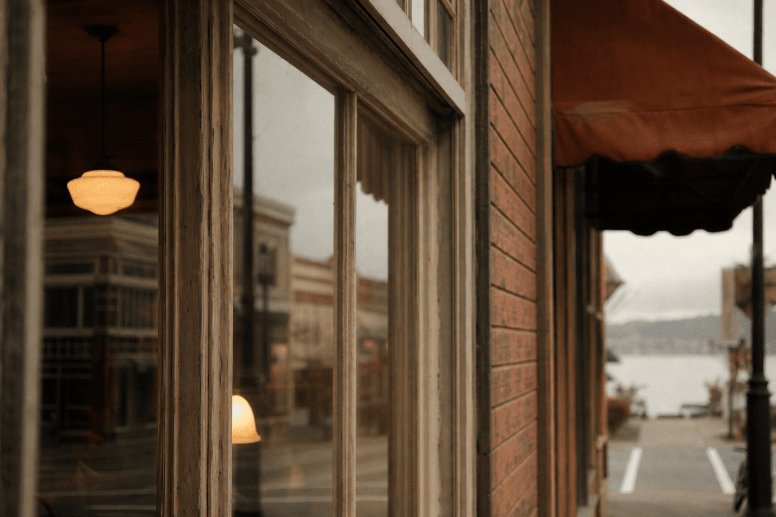 An Old Town Nanaimo café storefront, brick and warm awning, harbour reflected in the window.